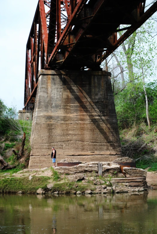 a man standing under an old rusted bridge