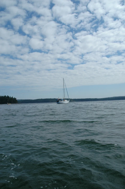 a sail boat traveling across a lake under a cloudy sky