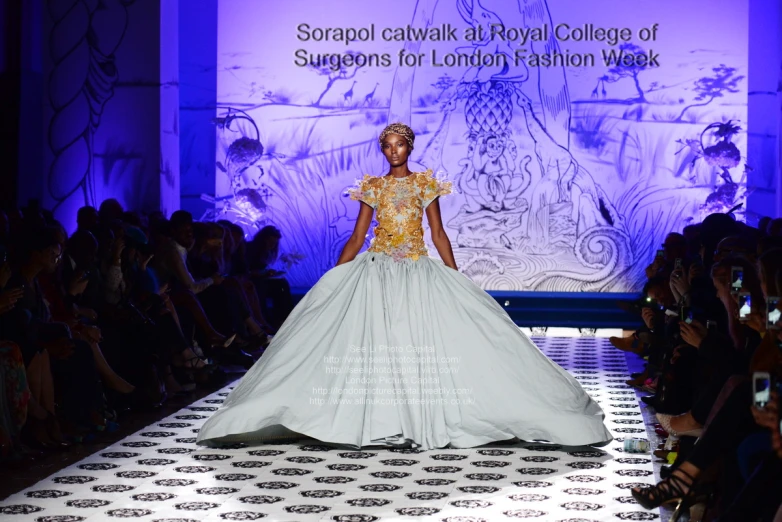 a woman in a white and blue gown walking down the runway