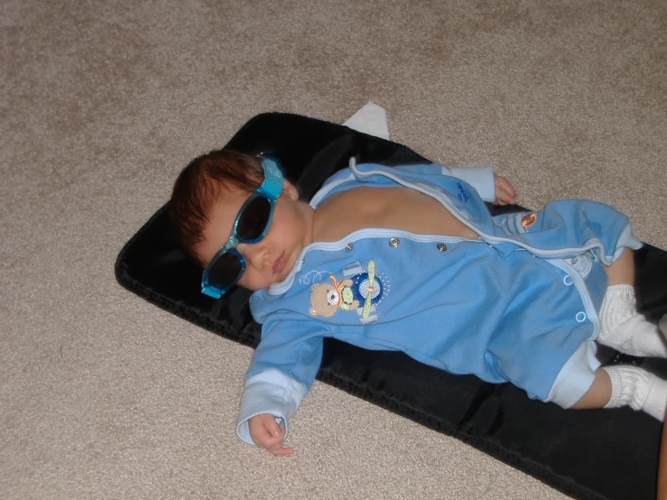 baby lying on pillow wearing blue sunglasses and white socks