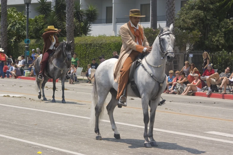 two men dressed in old - fashioned attire are riding horses with spectators in the background