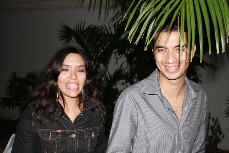 a couple poses for a picture in front of a palm tree