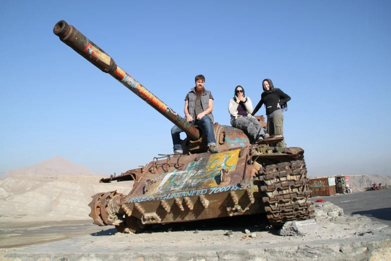 two men and woman standing on top of an abandoned tank