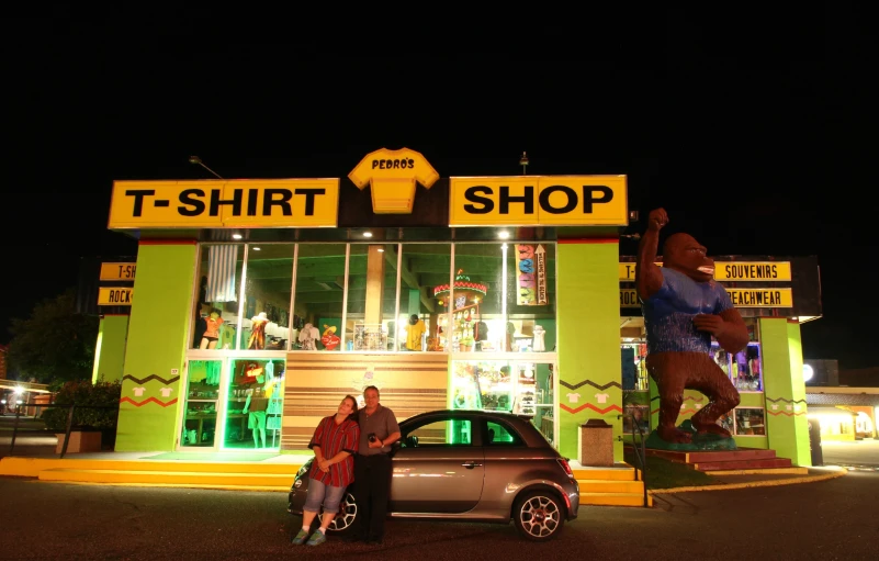 two people are posing in front of a t - shirt shop