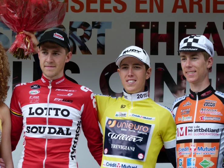three men on opposite sides of a podium one wearing yellow, the other red and white