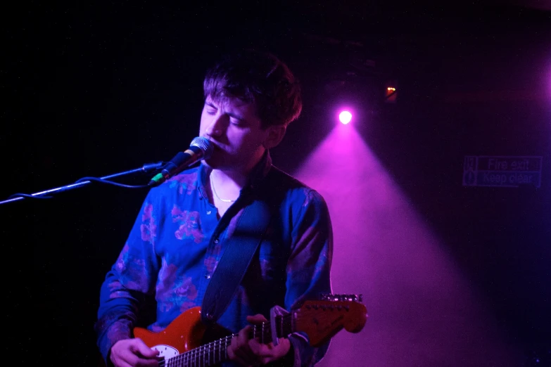 a young man holding a red guitar on stage