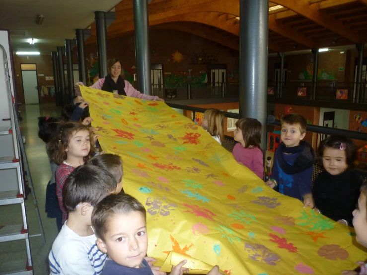 children are around an adult holding a yellow blanket