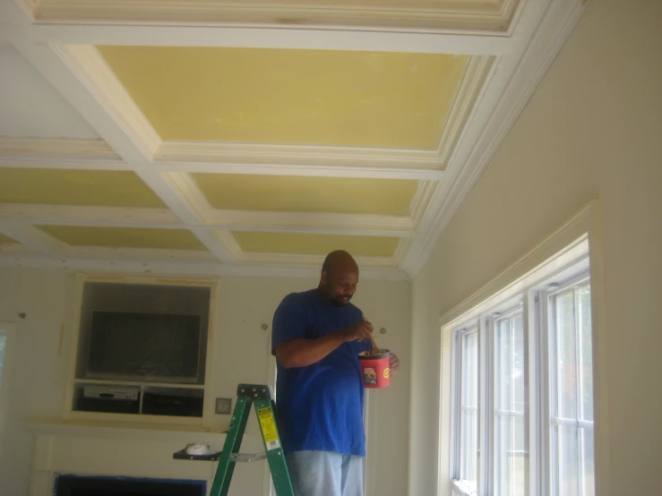 a man holding a can painting a room with a yellow ceiling