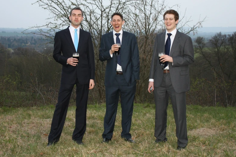 three men in suits and ties standing together on top of a hill