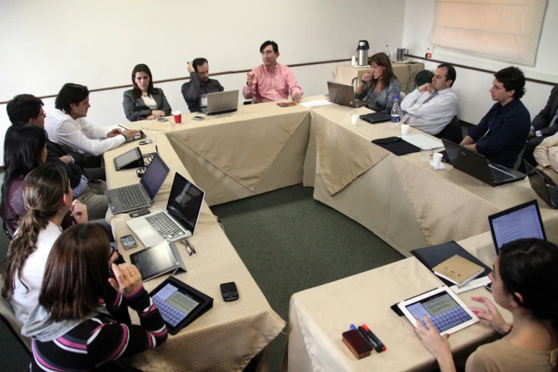 a group of people sit at a round table with laptops