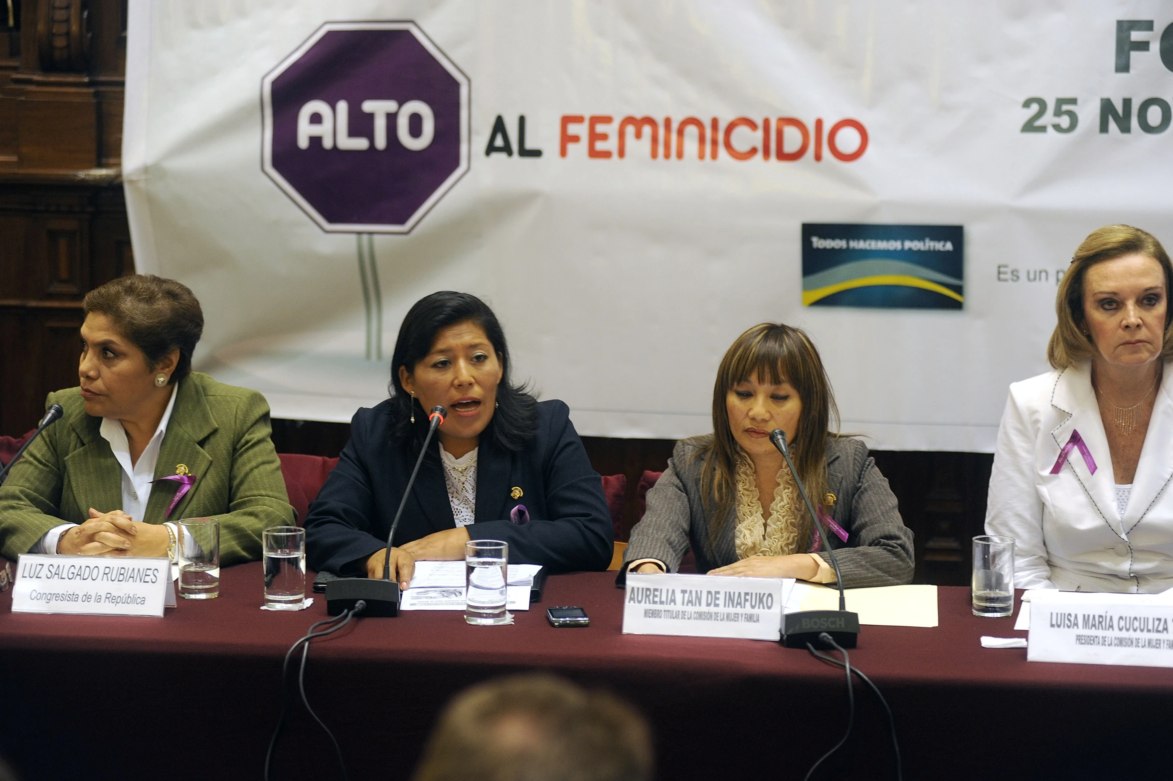 three women sitting at a table with microphones and two men standing in front