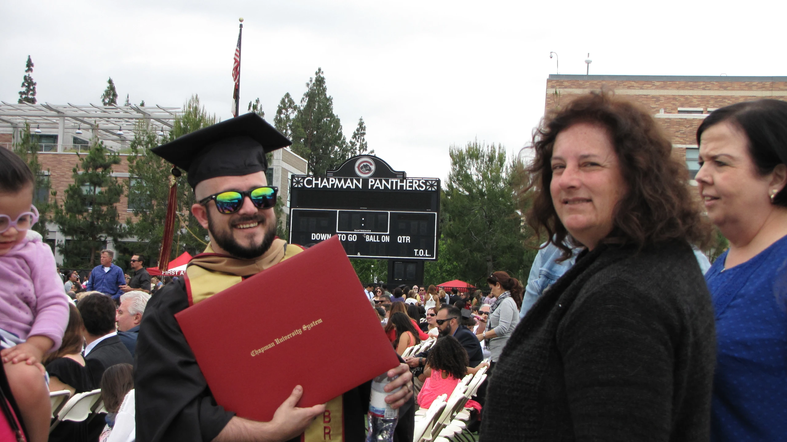 a man wearing a diploma stands next to a woman with sunglasses and a book