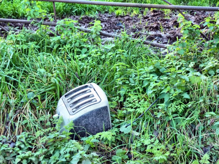 an old, dirty broken - down mixer laying in the grass near a power line