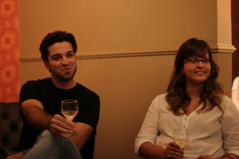 a man and woman sitting next to each other holding glasses of wine
