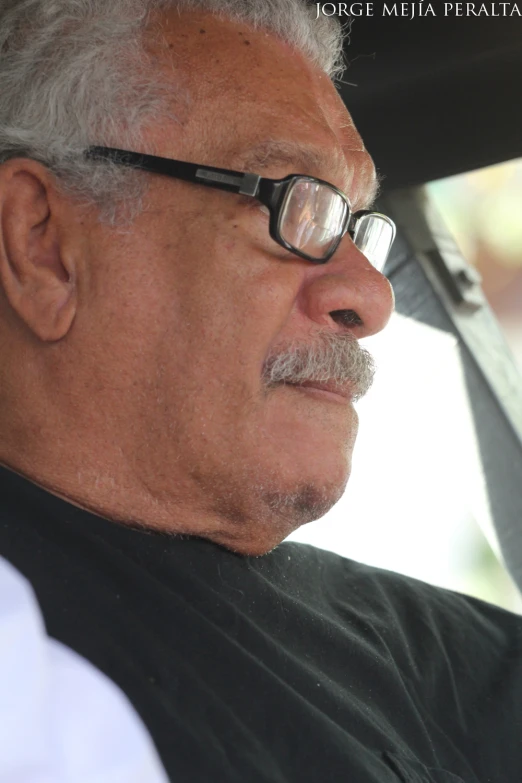 an older gentleman driving a car while wearing glasses