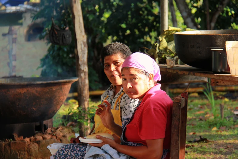 a woman and man are sitting outside near pots and pans