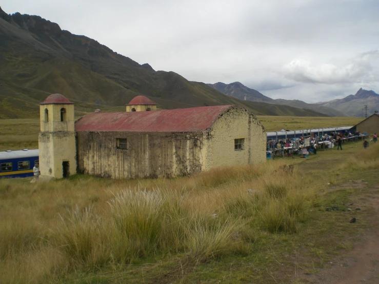 people walking along side an old building with mountains in the background