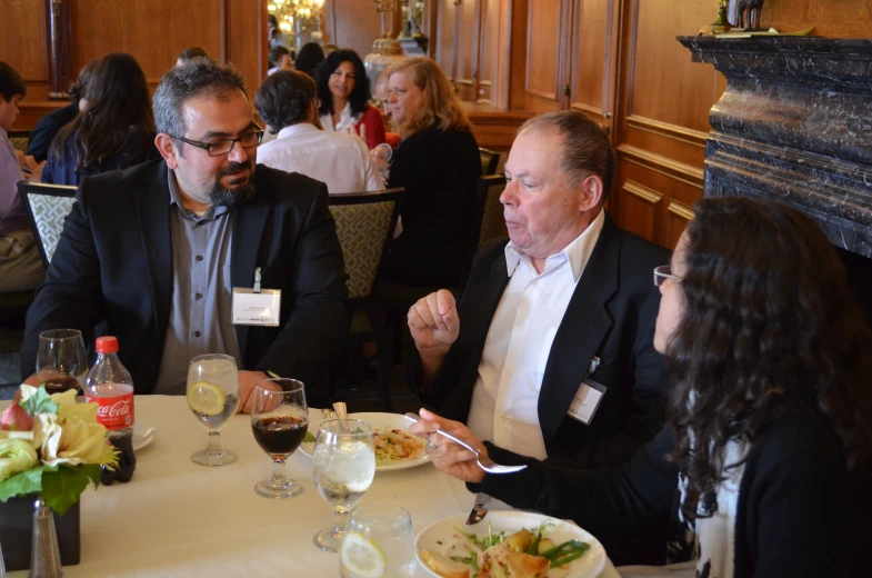 three people sitting at a dinner table talking and eating