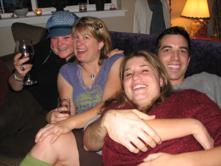 four people hugging on the couch with wine in glasses