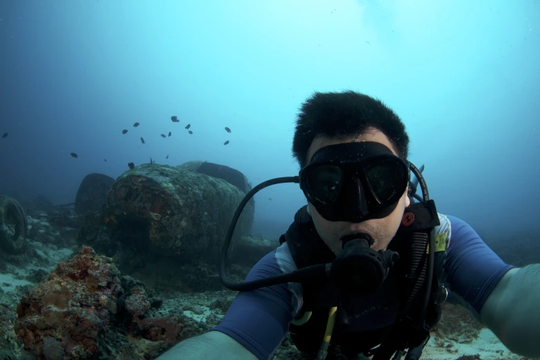 man scubas next to large coral reef wearing goggles