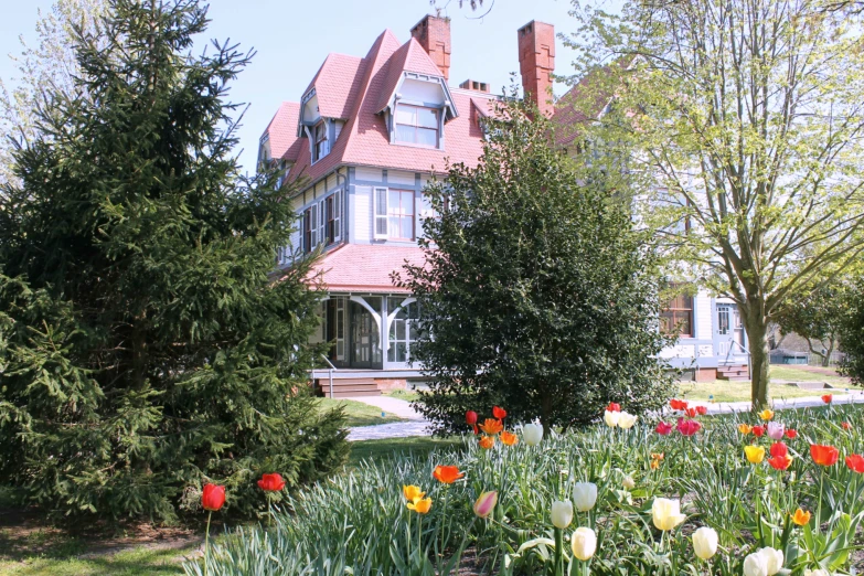 a large house in a flower garden next to trees