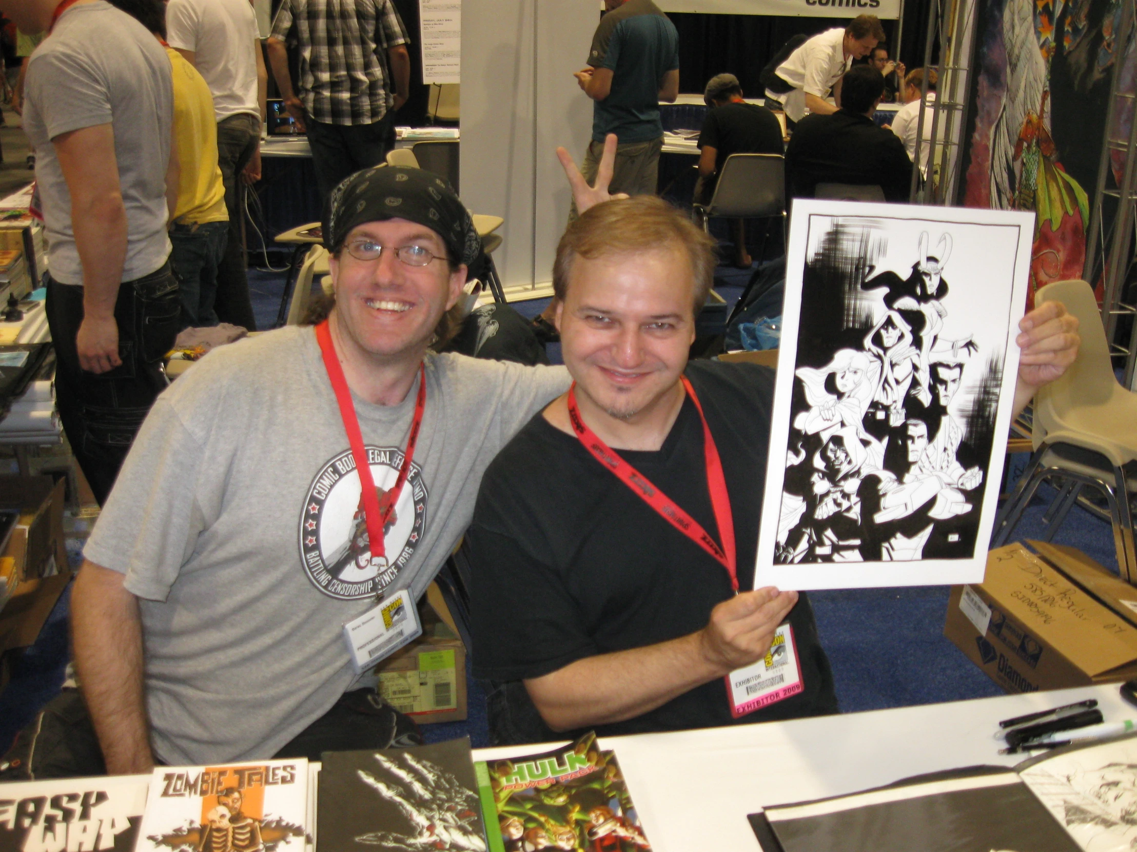 two men posing in front of a booth with posters