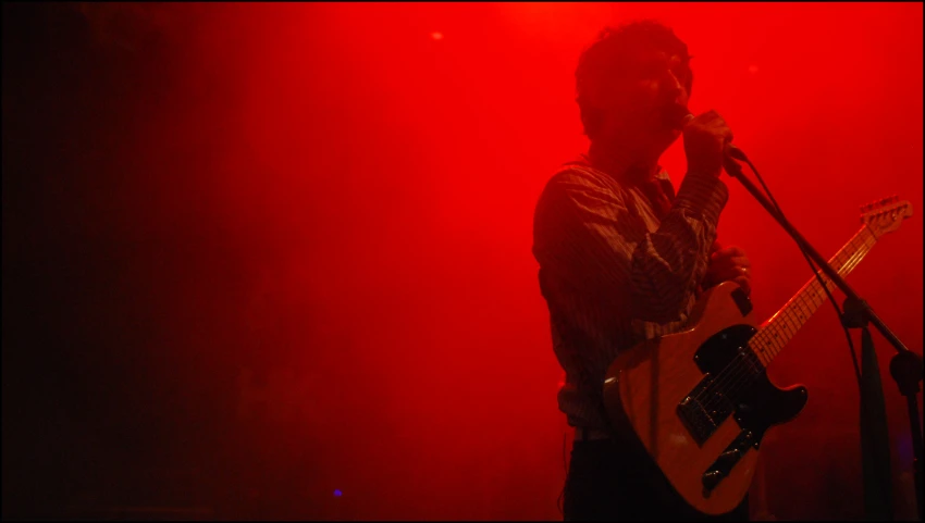 a person on stage holding a guitar with a microphone in the background