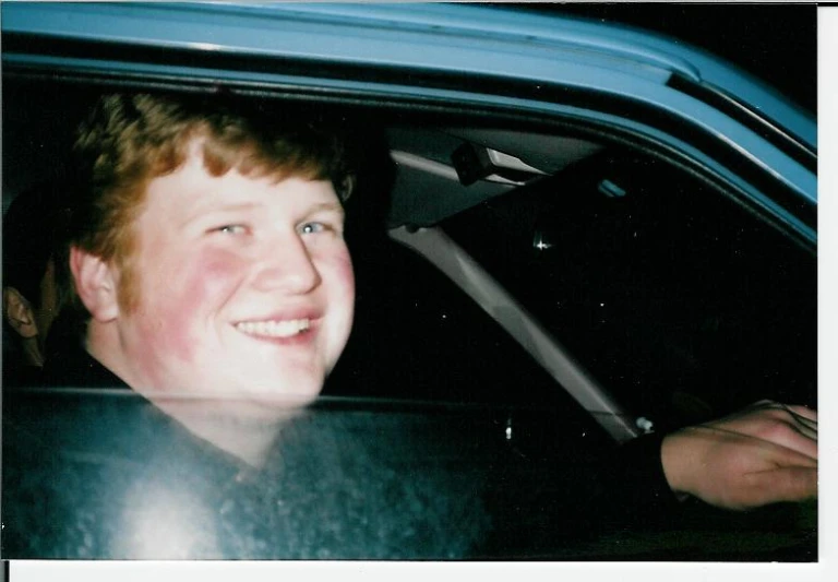 a boy smiling in his car with another person inside