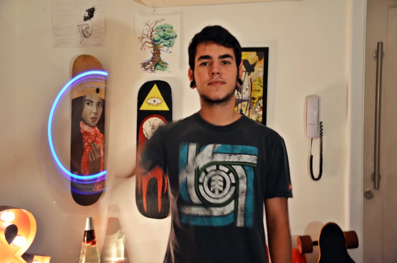 man in black shirt standing in living room with skateboard on the wall