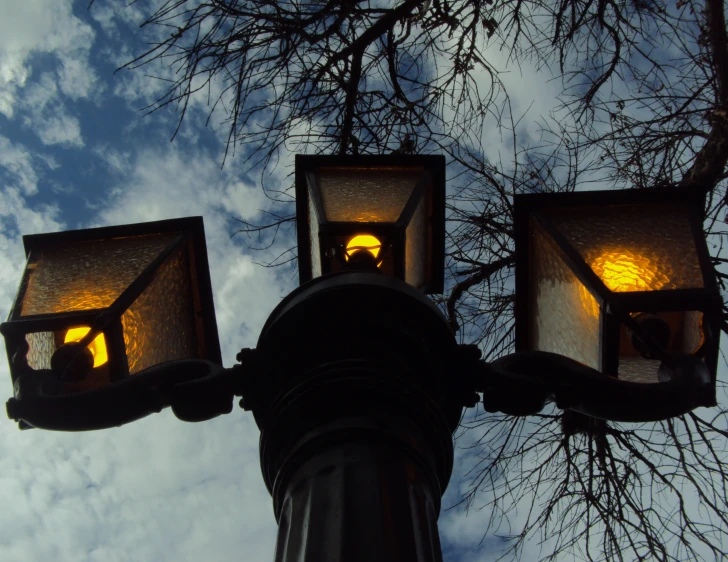 a lamp post with three lights on it and trees in the background