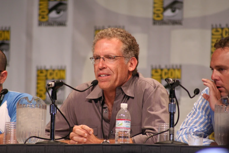 three men sitting at a table in front of microphones