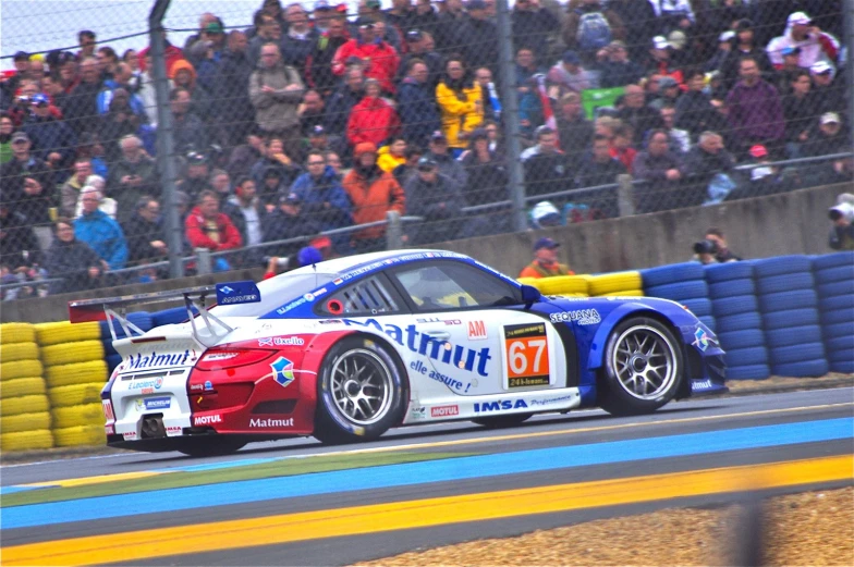 two cars driving down a track with spectators watching