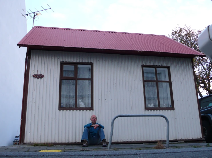 a man sitting on a curb next to a white building