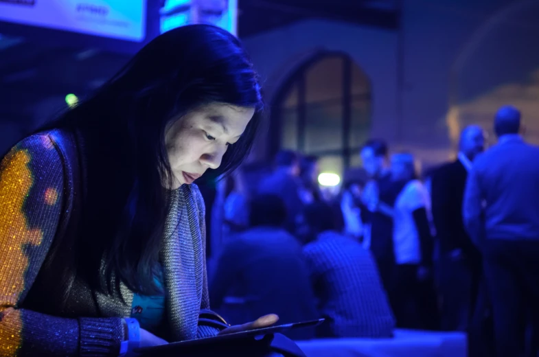 a woman looking at a device as she stands in a room full of people