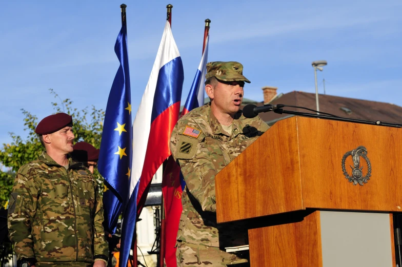 two soldiers in uniform stand behind a podium while another soldier speaks