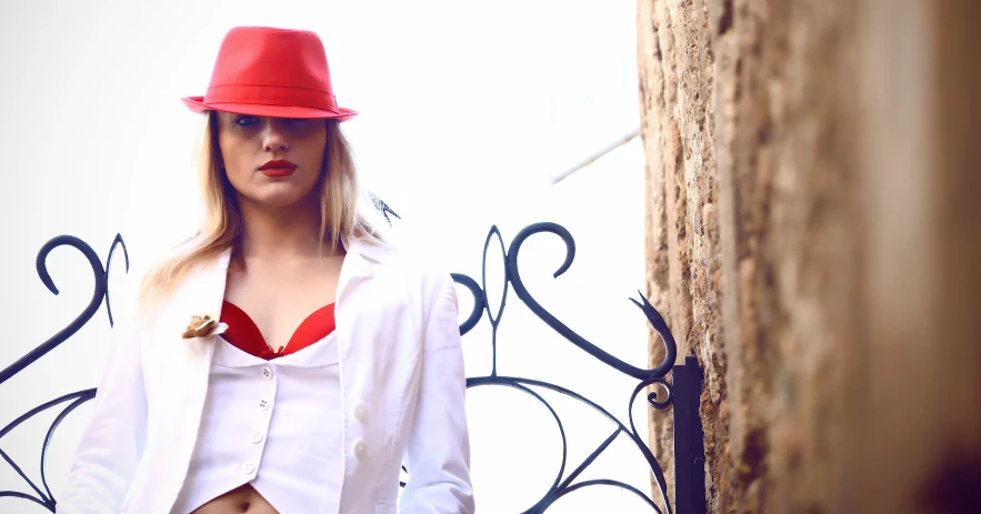 a young woman standing by a brick wall wearing a red hat