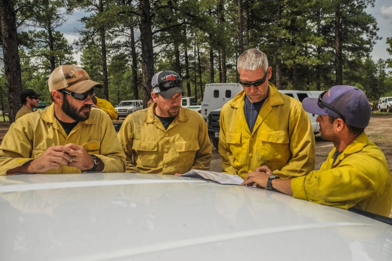 five fire fighters discussing a paper about what to do with an opened car hood