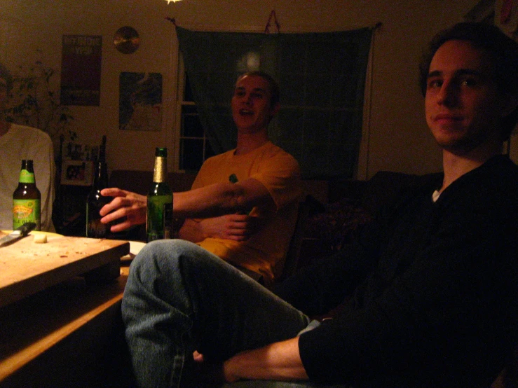 two men with beers at a table in a darkened room