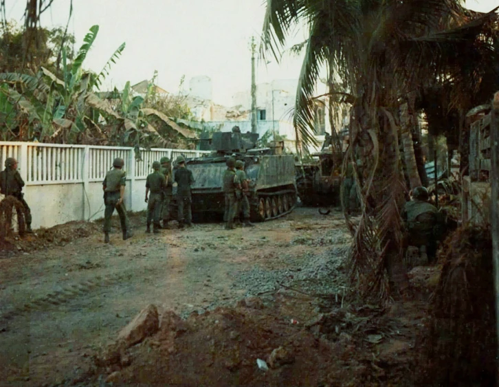 soldiers are walking near a tank in the middle of a dirt road