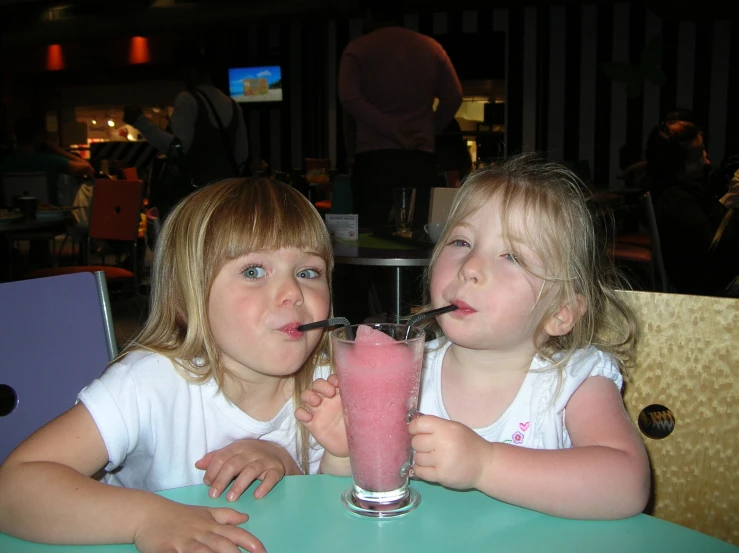 two little girls sitting at a table drinking soda