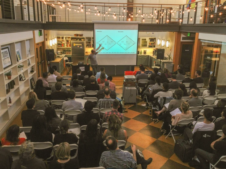 people sitting on chairs in a small room and one person in front of an projected screen is teaching the other person