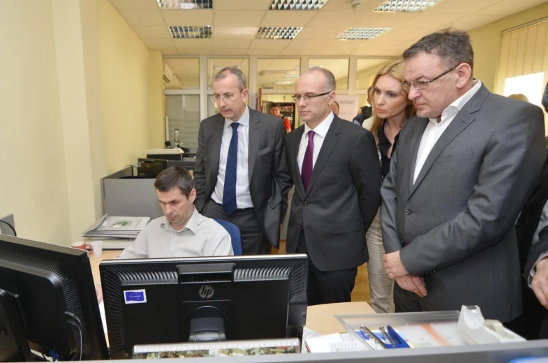 a bunch of people standing in front of two computer monitors