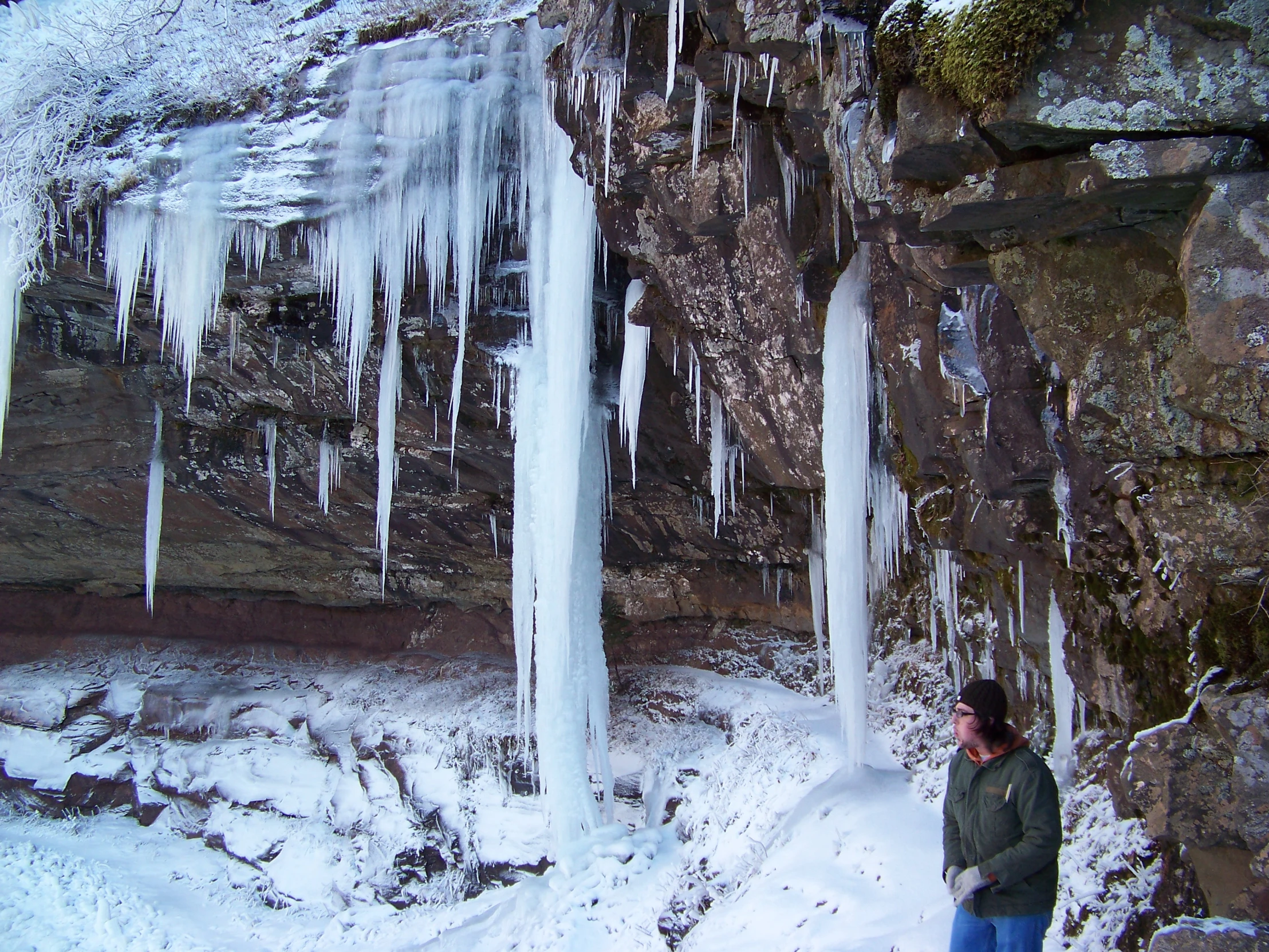 a woman standing next to a wall with ice and icicles on it
