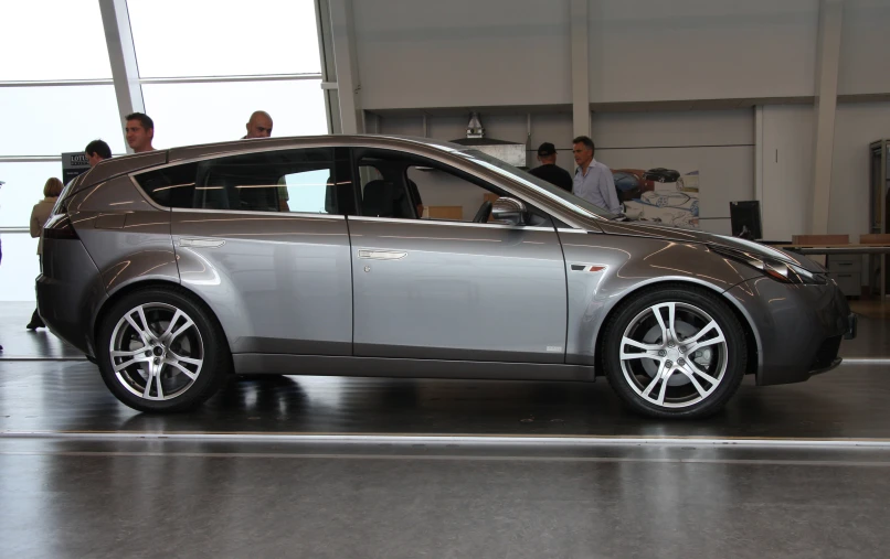 a silver car in a garage with people standing around