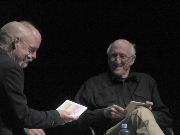 a person sitting in a chair handing another persons some paper