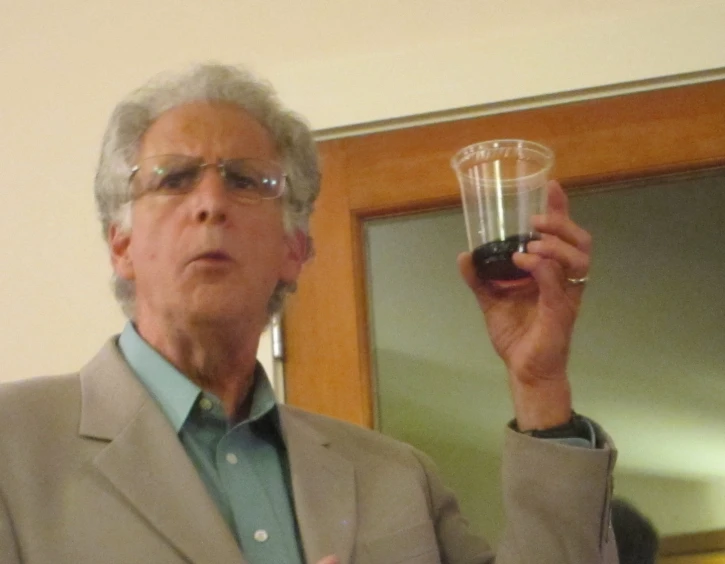 an older man in a suit holds up a plastic cup