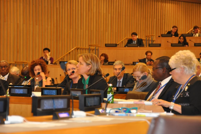 people sitting in rows in a conference room with one person pointing at the screen