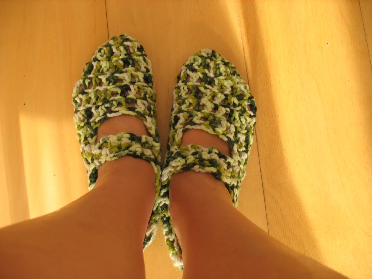 a pair of feet wearing crocheted slippers on top of wooden floor