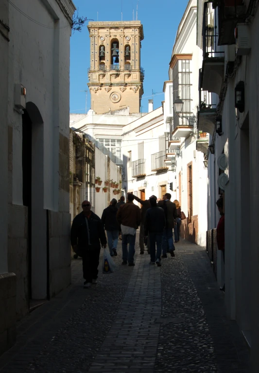 a group of people walk down an alley between white buildings