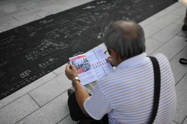 an old man is sitting on the ground reading a piece of paper